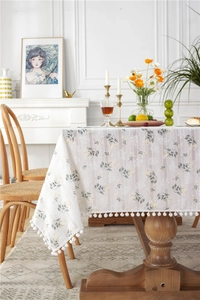 Detail of floral jacquard cotton tablecloth with decorative white pom-pom fringe trim