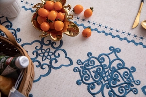 Detailed embroidery of blue geometric floral patterns on a beige cotton linen tablecloth