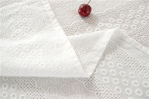 Detail of white cotton lace tablecloth with hollow-out floral embroidery and elegant drape
