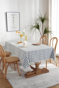 Close-up detail of green and white plaid tablecloth with white fringe tassels on wood