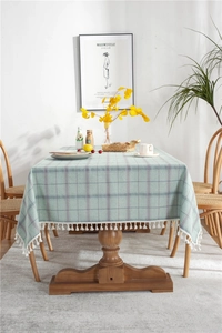 Close-up of light green plaid tablecloth with white fringe tassels on a dining table