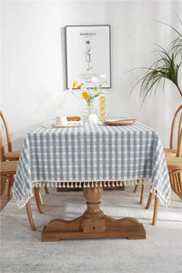 Close-up of light green and grey plaid tablecloth with white fringe tassels on wood table