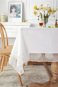 Detail of white cotton tablecloth showing intricate lace embroidery and tassel edges