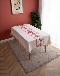Close-up of red floral embroidery and tassel fringe on a beige linen tablecloth