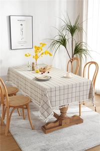 Detail of checkered beige cotton linen tablecloth featuring white decorative tassels fringe
