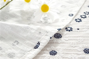 Detail of sunflower jacquard fabric with embroidered daisy patterns on white cotton