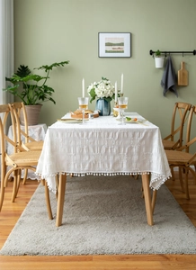 Detail view of white rectangular cotton tablecloth with textured patterns and pom-pom trim