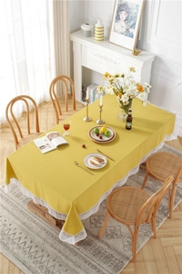 Macro shot of yellow cotton tablecloth with white lace tassel fringe on a wooden table