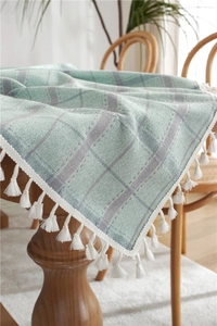 Detail of mint green and grey plaid linen tablecloth featuring elegant white tassels