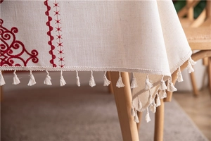 Detail of embroidered floral patterns and cotton tassels on off-white linen tablecloth
