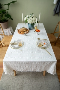 Close-up of white cotton tablecloth featuring pom-pom fringe and textured square weave