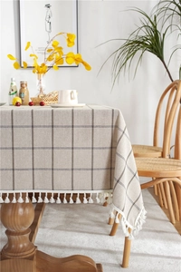 Detailed view of beige plaid tablecloth with white fringe tassels on a wooden table