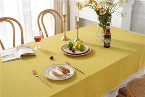 Detail of mustard yellow cotton tablecloth featuring elegant white lace edges and texture