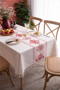 Close-up of beige tablecloth with red floral embroidery and delicate woven fringe edges