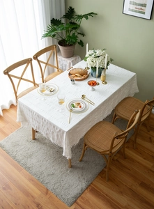 Detail of white cotton tablecloth with textured floral patterns and small pompom tassels