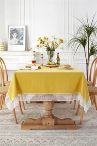 Detail of solid yellow cotton tablecloth featuring elegant white lace edges and rustic texture