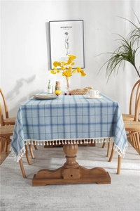 Detailed close-up of blue geometric plaid tablecloth featuring white cotton ball tassels