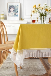 Detail view of ginger yellow cotton tablecloth with white lace floral trim on the edge