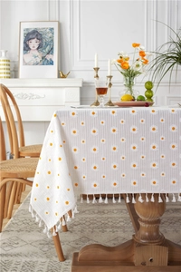 Detail of white cotton tablecloth showing yellow daisy embroidery and white fringe trim