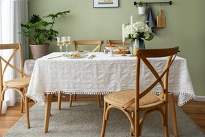 Close-up of white rectangular tablecloth with jacquard checkerboard texture and pompom fringe