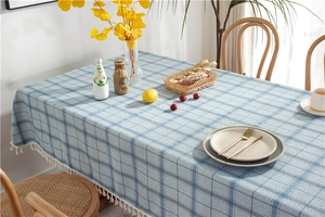Detail of blue plaid tablecloth with white fringe tassels on a wooden dining table