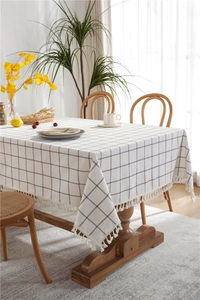Close-up of minimalist black grid tablecloth with white cotton fringe tassels on a wooden table