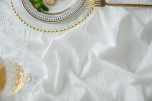 Macro view of white cotton tablecloth featuring 3D tufted jacquard texture and elegant trim