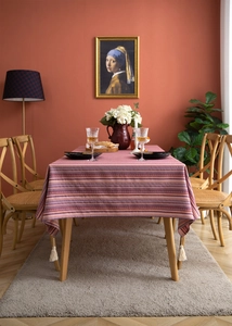 Detail of bohemian red striped tablecloth with white tassels on a vintage wooden dining table