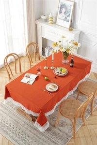 Detail of brick red cotton tablecloth featuring elegant white lace edges and texture