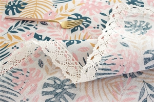 Detail of tropical leaf print tablecloth with elegant white lace border and fabric texture