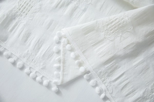 Detailed view of white cotton tablecloth fabric with jacquard texture and pom-pom trim