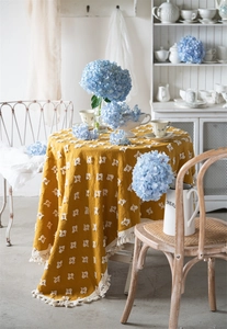 Detail of vintage ginger yellow cotton tablecloth with white tufted squares and thick fringes