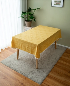 Close-up of yellow rectangular tablecloth featuring white tassel pom-poms and jacquard texture