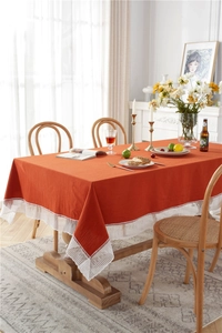 Detail of orange washed cotton tablecloth featuring elegant white lace edge on a wood table