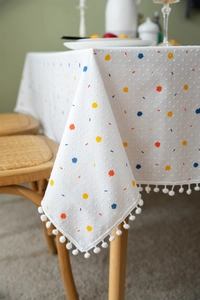 Close-up of white cotton tablecloth with colorful dots and decorative pom-pom fringe edges