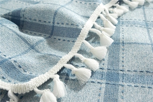Macro detail of blue plaid table cloth featuring white tassels and woven texture