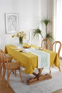 Detail of yellow tablecloth with ruffled edges and patterned table runner with white tassels