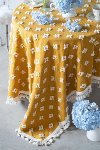 Detailed close-up of yellow jacquard tablecloth with white tufted squares and tassel trim