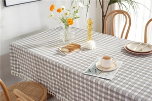 Detail of khaki plaid tablecloth featuring elegant white tassel fringes on a wooden table
