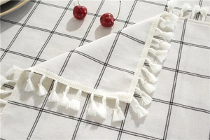 Detail of grid pattern cotton linen tablecloth with white decorative fringe tassels