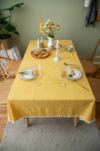 Detailed view of yellow rectangular cotton tablecloth with 3D jacquard and white pom-pom trim