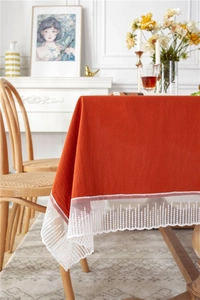 Detail of terracotta cotton tablecloth with white lace edges in a rustic dining room