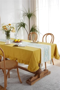 Detail of yellow tablecloth with ruffled edge and geometric table runner with tassels