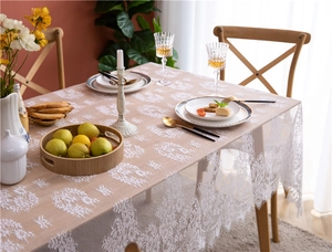 Detail of white French floral lace tablecloth with elegant scalloped edges on a wooden table