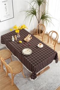 Close-up of brown plaid table cloth with white tassels on a wooden dining table