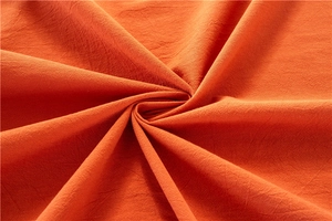 Macro shot of orange washed cotton tablecloth fabric showing soft texture and radial folds