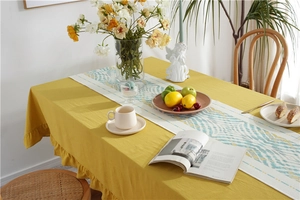 Detail of yellow cotton tablecloth with ruffled edges and green geometric table runner