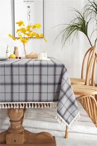 Detailed view of grey checkered linen tablecloth with white decorative tassels on wood table