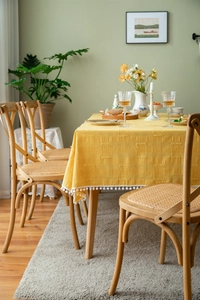 Detail of yellow cotton linen tablecloth featuring square textures and white pompom fringe