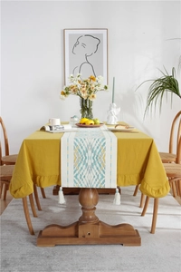 Detail of yellow ruffled tablecloth with teal geometric runner and white tassels on wood table